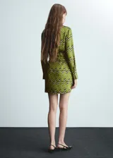 Vestido corto de tejido fluido color verde con estampado abstracto en blanco y negro. Diseño cruzado con cuello camisero, mangas largas y cierre de lazo lateral.