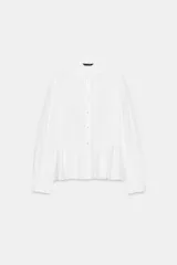 Camisa blanca de popelín con cuello redondo con volante y lazo, manga larga y bajo peplum. Cierre frontal con botones.