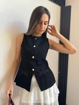 Chaleco negro de denim con corte peplum, cuello redondo y cierre frontal con botones dorados.