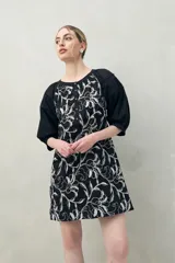 Vestido corto negro con bordado floral blanco, escote redondo con abotonadura frontal y mangas 3/4 abullonadas con pliegues en los hombros.