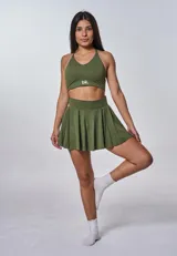 Conjunto deportivo verde militar compuesto por un top con breteles cruzados en la espalda y una minifalda plisada. El top tiene el logo 'bk.' estampado en blanco. Incluye calcetines blancos.
