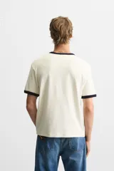 Camiseta azul marino de corte recto, con cuello redondo y mangas cortas. Presenta ribete blanco en cuello y mangas.