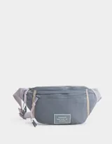 Riñonera gris de tela deportiva con correa regulable color lila. Tiene cierre superior con tirador de cordón y goma, bolsillo frontal con cierre y etiqueta de goma con la inscripción "Brooklyn New York - NY Est. 1970".