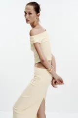 Falda midi color crema, de tiro alto con cintura elástica y detalle de pliegues laterales.
