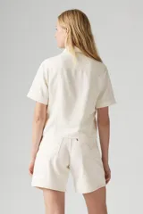 Camisa color crema de manga corta con cuello clásico, cierre frontal con botones y dos bolsillos con solapa en el pecho.