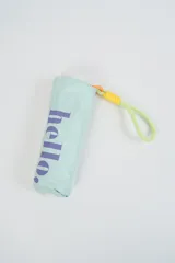 Paraguas plegable de color beige claro con la palabra "hello." estampada en azul. Incluye un asa de mano tipo correa en tonos amarillo y rosado.
