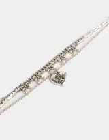 Collar corto plateado de tres capas: una de strass, otra con dijes de moños y una tercera con un dije de corazón con detalles grabados.