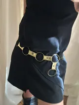 Cinto dorado con apliques de cuero y aros metálicos.