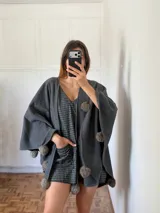 Ruana gris con pompones en el borde.