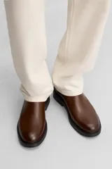 Bota Chelsea marrón de cuero, con elásticos laterales y tirador trasero. Suela negra con ligero tacón.