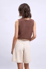 Chaleco de tejido de punto color crudo, sin mangas, con escote en V y cierre frontal de botones marrones.