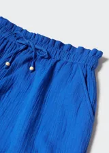 Conjunto de short y top azul eléctrico de tela arrugada. El top tiene tirantes anchos con volantes y escote recto. El short tiene cintura elástica con cordón ajustable y bolsillos laterales.