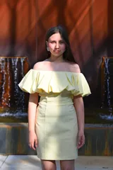 Vestido corto color amarillo manteca, con escote off-shoulder con volados y falda ajustada.