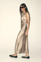 Vestido largo de satén color champagne, con escote en pico, tirantes anchos cruzados en la espalda y ribetes negros en contraste.