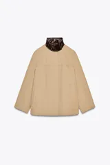 Cazadora color beige con cuello alto en tejido efecto piel marrón a contraste. Manga larga, bolsillos delanteros, detalle de pespuntes a tono, forro interior y cierre frontal con cremallera y botones a presión ocultos por solapa.