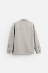 Camisa color crema de corte relaxed fit, confeccionada en tejido de mezcla de algodón suave al tacto. Tiene cuello solapa, manga larga con puños abotonados, un bolsillo de parche en el pecho y cierre frontal con botones.