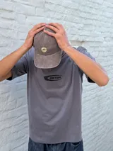 Remera gris de corte oversize con cuello redondo y manga corta. Estampado frontal con el texto "OSTEN" en negro con un diseño estilizado.