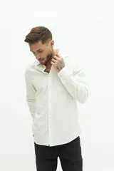 Camisa blanca de manga larga texturizada, tejida en dobby, con cuello italiano y cartera abotonada. Tiene un logo bordado en el pecho.