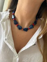 Collar corto con cuentas irregulares de resina azul con efecto marmolado, intercaladas con cuentas pequeñas de coral rojo.