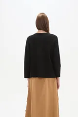 Sweater blanco liso, de corte holgado, con cuello a la base y broches decorativos en los laterales.