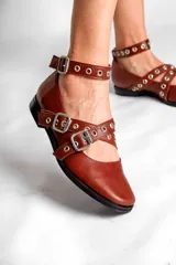Chatas de cuero color marrón con tiras cruzadas con hebillas y tachas plateadas.
