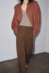 Pantalón marrón de tiro medio con trabillas en la cintura, bolsillos laterales, pinzas delanteras y bajo ajustable con trabilla y botón.