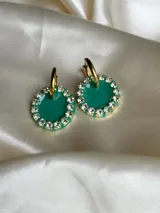 Par de aros colgantes con dije circular de resina con glitter multicolor y borde de strass. El arito es de acero quirúrgico dorado.