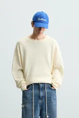 Jersey color crudo de algodón con textura, corte relaxed fit, cuello redondo y manga larga. Acabados en rib con detalle de vuelta.