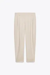 Pantalón color beige de tiro alto con bolsillos delanteros, cierre frontal con cremallera y botón, y ruedo con vuelta.