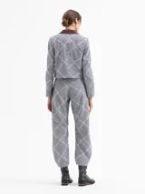 Pantalón de corte mom fit confeccionado en tejido con diseño de microcuadros y bordado de labios en color celeste que forman un patrón de rombos. Presenta una cintura con efecto de cinto integrado, bolsillos laterales con detalles en cuero color borravino y pinzas en las rodillas que aportan volumen. El cierre es mediante gancho, botón interno y cremallera.