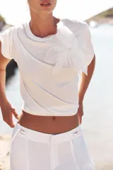 Camiseta blanca de algodón con cuello redondo, manga corta y detalle de flor de organza con strass en el frente.