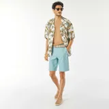 Camisa de manga corta blanca con estampado de hojas en tonos marrones, verdes y amarillos. Tiene cuello clásico, cierre frontal con botones y corte recto.