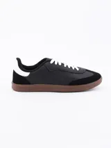 Zapatillas urbanas negras con cordones blancos y suela marrón.