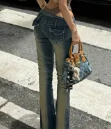 Jean tiro bajo de mezclilla azul con efecto gastado y paneles con costuras curvas que recorren las piernas. Presenta cierre frontal y corte ligeramente acampanado en la botamanga.