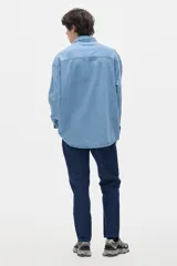 Camisa de jean celeste con botones negros y pespuntes a contratono. Tiene corte oversized y mangas largas con puños abotonados.