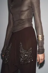 Brazalete rígido abierto de metal dorado envejecido, con textura martillada y detalles en relieve de flores y figuras. Presenta incrustaciones de piedras de resina en tonos tierra, morados y verde menta.