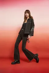 Campera de jean negra de corte holgado con detalles de tachas plateadas en costuras, hombros y puños, y bordado floral blanco en las mangas.