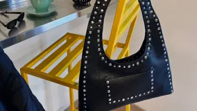 Cartera negra tipo hobo de ecocuero con tachas plateadas y bolsillo frontal.