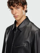 Campera de cuero negra con cuello camisero y cierre frontal. Presenta múltiples cierres metálicos en el frente, incluyendo uno diagonal en el pecho y dos bolsillos laterales.