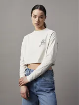 Remera cropped color beige de algodón, con cuello redondo y mangas largas. Presenta el logo de Calvin Klein Jeans estampado en el pecho.