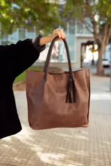 Bolso tote de cuero color marrón con asas de cuero negro y detalle de borla de cuero negro.