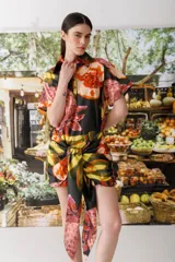 Vestido camisero corto con estampado abstracto en tonos naranja, rosa, amarillo y negro. Tiene cuello camisero, mangas cortas y cierre frontal con botones. Incluye lazo en la cintura para ajustar.