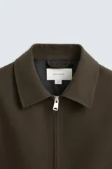 Sobrecamisa negra de lana con cuello solapa, manga larga con puños abotonados, bolsillos de vivo en la cadera y cierre frontal con cremallera.