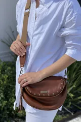 Bandolera marrón confeccionada en cuero vacuno, con cierre superior y correa regulable de cinta. Forrada en tela de algodón, con bolsillo interno con cierre y bolsillo trasero con cierre.