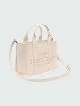 Bolso tote pequeño de cuero texturizado color gris con doble asa corta superior y correa larga extraíble y ajustable para llevar al hombro. Estampado frontal con el texto "The Tote Bag" y el nombre de la marca.