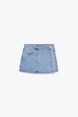 Minifalda pantalón de tiro alto confeccionada en denim celeste, con bolsillos delanteros y traseros. Presenta cierre frontal cruzado con cremallera oculta y botón metálico.