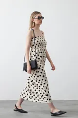 Vestido midi de silueta fluida con estampado de grandes lunares negros sobre fondo beige. Cuenta con un cuerpo fruncido elástico tipo nido de abeja, escote recto y tirantes finos regulables que se anudan en los hombros.