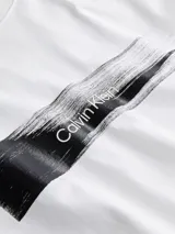 Remera blanca de algodón regenerativo con cuello redondo y logo de Calvin Klein en el pecho con efecto de pincelada negra.
