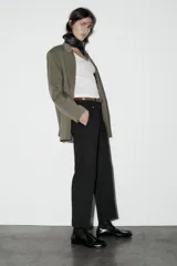 Pantalón de vestir color beige, de tiro alto y corte recto. Incluye cinturón marrón con hebilla metálica. Presenta bolsillos laterales y falsos bolsillos traseros de doble vivo. Cierre frontal con cremallera, botón interior y gancho oculto.