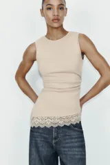 Camiseta ajustada (slim fit) de cuello redondo y manga sisa, color beige claro, con frunces laterales y bajo asimétrico con terminación de encaje a tono.